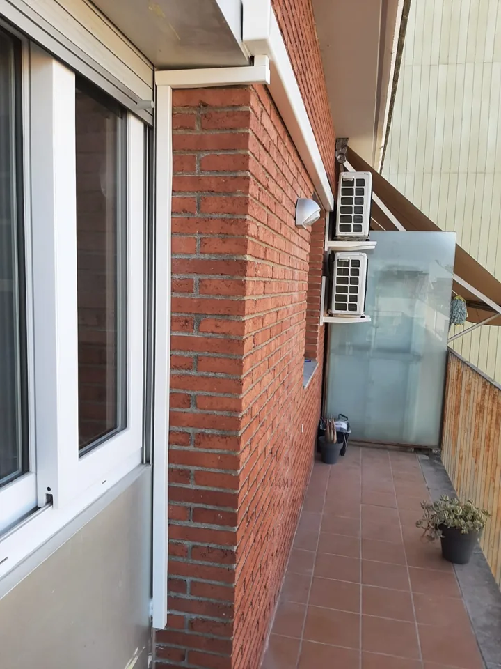 Dos unidades exteriores de aire acondicionado montadas en una fachada de ladrillo junto a un balcón